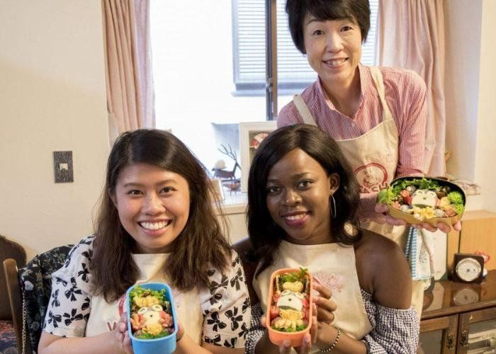 A host and two guests smiling at the camera, showing off their cute kyara bento boxes.